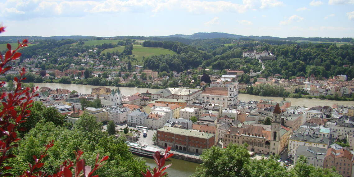 Luftaufnahme von Schärding mit Fluss Inn, historischen Gebäuden und umliegenden Hügeln.